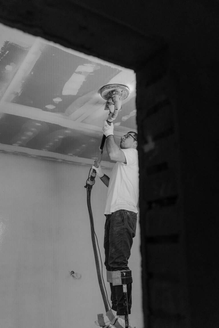 Man sanding the ceiling during a house renovation in black-and-white.